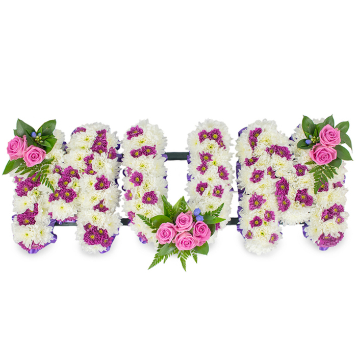 This thoughtful floral tribute reads MUM in three-dimensional capital letters, each hand-formed from a dense carpet of immaculate white chrysanthemum florets that give the piece a soft, cloud-like texture and a sense of quiet dignity. Dotted through the pristine white are accents of magenta and lavender pom-pom blooms which create a gentle, melody-like pattern and lend visual depth without overpowering the pale field. The composition is punctuated by three rose clusters in a warm pink tone: a small, elegant pair at the upper left of the first M, a more luxurious cluster of several spray roses tucked into the lower curve of the U, and a mirrored grouping at the upper right of the last M. Ferny fronds and deeper green foliage cradle each rose cluster, introducing natural movement and a sombre richness, while tiny blue accent flowers shine like delicate beads among the petals. Along the edges a narrow purple ribbon subtly outlines the letters, enhancing definition, and a faint dark horizontal bar links them together to suggest stability and cohesion. Photographed against a plain white ground with soft side lighting, the tribute reads as both an expression of mourning and a celebration of memory. Familiar to neighbours around Chinbrook Meadows and Downham, this style of personalised funeral tribute embodies the attentive craftsmanship and quiet sympathy families seek when honouring a mother or matriarch.