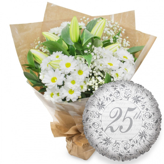 Against a pristine white background, a classic Silver Anniversary arrangement is carefully presented, combining a white floral bouquet with a single shimmering balloon. The bouquet, poised to the left, is composed primarily of white chrysanthemum flowers, each one daisy-like with a ring of crisp, narrow petals around a warm yellow centre. These blooms cluster together to create a generous, rounded shape, giving the impression of abundance and gentle celebration, much like a family gathering in a Grove Park garden. Slender white lily buds stand tall amid the chrysanthemums, their smooth petals folded in on themselves, edged subtly with a cool green hue that hints at the freshness of early morning. Between these focal flowers, thin stems of white baby's breath diffuse into tiny blossoms, creating a veil of softness and a slightly clouded texture around the arrangement. Lush dark green leaves sit behind and among the blooms, some arching outward and others tucked within, offering a strong, natural backdrop that emphasises the purity of the white petals. The stems are carefully encased first in a sleeve of clear cellophane, then wrapped in rustic brown kraft paper, the edges folded into neat angles and tied at the base, suggesting the bouquet has just been finished at a local Grove Park florist bench and is ready to be carried along quiet residential streets. To the right of the bouquet, a round silver foil balloon rests, its metallic surface gently reflecting the light. The balloon is decorated with an ornate border of scrolling lines and stylised floral shapes in darker silver, framing a central 25th picked out in elegant script. Behind the main design, the words Happy Anniversary softly repeat in pale grey across the surface. Together, the bouquet and balloon create a scene of understated elegance and heartfelt celebration for twenty-five years of shared life.
