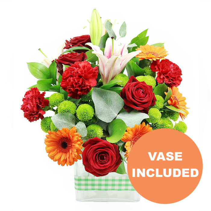 A vibrant, mixed-colour bouquet fills a low rectangular glass vase, creating a lively focal point that stands out against a spotless white background. The vase itself is finished with a light green and white gingham ribbon wrapped around its lower half, lending a relaxed, homely character that suits many Grove Park interiors. Above this, the flowers are tightly massed into a rounded, almost dome-like form. Deep crimson red roses, with velvety, densely layered petals, anchor the design and provide a rich, romantic base tone. Interspersed, soft, frilled red-orange carnations echo the warmth of the roses but introduce a cloud-like texture. Bright orange gerbera daisies, each with a dark brown or black centre and a ring of bold, flat petals, face outward at slightly different angles, creating a sense of movement and visual rhythm. Piercing through the bouquet, white Oriental lilies rise higher; some trumpet-shaped blossoms are fully open, displaying delicate pink stripes within their petals and dustings of pollen on visible stamens, while others remain in bud, adding elegance and anticipation. Threaded between the larger blooms are clusters of lime-green pompom chrysanthemums, their tiny rounded heads adding both a lively burst of colour and playful dimension. The composition is enveloped in lush foliage: broad, glossy dark green leaves and slender stems of silvery eucalyptus that curve gently around the outer edges, introducing soft, cool notes and a hint of woodland freshness. At the lower right of the image, a circular orange disc partially overlaps the vase, clearly marked with the words VASE INCLUDED in bold white capitals, communicating that no extra container is needed. The bouquet radiates a mood of cheerful celebration, ideal for deliveries across Grove Park-from riverside apartments off Burlington Lane to quiet side streets near the station-whenever there is a need to say happy birthday, congratulations, or simply thinking of you.