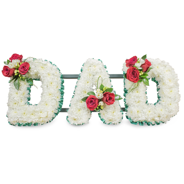 A carefully engineered sympathy composition that reads DAD in large, hand-shaped letterforms, each formed from a dense carpet of tiny, pure white chrysanthemum heads to give a velvety, uniform texture and a quietly luminous surface. The perimeter of each letter is trimmed with a deep emerald green pleated ribbon, providing contrast and a clean, architectural edge that makes the letters read clearly from a distance. Placed with floral discipline, three accent sprays - one on the upper left curve of the first D, one set within the left diagonal of the A, and one on the upper right of the final D - combine deep red roses in varied stages of opening with clusters of white freesia and abundant green foliage; occasional lisianthus buds or slender bear grass strands add delicate punctuation and movement. A narrow, unobtrusive framework of dark green or black metal bars links the letters behind the blooms, invisible at first glance but essential for stability during procession or display at a funeral venue. The lighting here is even and soft, allowing the whites to read pure and the reds to appear saturated without glare, while the mixed fragrances of roses and freesia offer a steady, comforting note. As an experienced local florist might explain when advising families in Grove Park, Horn Park or Downham, this arrangement is intentionally classic - combining symbolism, durability and tasteful composition - so it sits respectfully in a chapel, crematorium or graveside setting and speaks of devoted love and profound respect for a father.