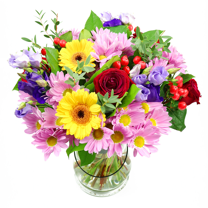 A vibrant mixed-flower bouquet stands tall in a transparent glass vase, set against a bright white background that accentuates its colourful, garden-fresh character. The arrangement is shaped in a full, domed style, with blooms densely clustered so that no space feels empty, conveying generosity and abundance. At the heart of the composition, rose heads in a deep, velvety red open outward in layered spirals, lending a sense of passion and timeless elegance. Close by, two golden yellow gerbera daisies with dark brown-orange centres tilt slightly, their clean, bold petals forming perfect circles that radiate cheerful positivity. Around these, a soft collar of pink and pale lilac daisies or chrysanthemums spreads gently, each flower featuring numerous slender petals and a neat yellow centre, adding lightness, texture, and a soothing pastel glow. Intermixed with these blooms are stems of lisianthus in shades of purple and lavender, their bell-shaped flowers and softly ruffled edges bringing a cool, graceful contrast to the warmer tones. Glossy red hypericum berries appear between the petals, clustered in small groups like tiny, polished beads, providing a striking textural twist and a hint of festivity. The bouquet is woven through with greenery - some leaves broad and dark, adding structure, others finer and lighter, curling outwards to create movement and a sense of natural growth. Within the glass vase, the stems are visible, cut to different lengths but arranged neatly in clear water, highlighting the florist's experienced hand. The overall effect is joyful yet refined, ideal as a gift for birthdays, anniversaries, or simple thank-yous in Grove Park, whether placed on a sunny windowsill near the common or delivered to a cosy home along the quiet residential streets that define the neighbourhood.