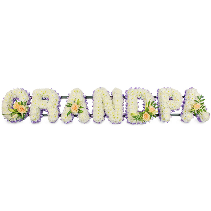 A custom funeral flower arrangement spells out the word GRANDPA in large, block letters, capturing both presence and tenderness in a single composition. The letters are arranged horizontally in a neat line, suggesting they are designed for display at a graveside, cremation chapel, or church service in Grove Park. Each letter is generously covered with small white chrysanthemums or similar delicate blossoms, arranged so densely that the eye reads only soft, ruffled petals rather than any underlying structure. The chrysanthemums form a plush, almost velvety field of white, lending the tribute an air of purity and calm remembrance.   

Along the perimeter of every letter runs a slender border of light lavender or lilac flowers, producing a fine, coloured edge that frames each character and prevents it from visually blending into its surroundings. This pastel purple fringe adds a cool, soothing tone to the piece, echoing the quiet atmosphere of tree-lined streets and calm corners of Grove Park. Interspersed among the white blooms are carefully placed accent clusters on the G, first A, D, and the final A. These clusters feature peach roses in various stages of opening, from tight buds to softly cupped flowers, their warm apricot petals offering a gentle contrast to the white chrysanthemums.   

Nestled around the roses are touches of lush green foliage and a few slender white buds that hint at lilies just about to open, adding subtle height and interest without overwhelming the design. All seven letters are supported on a narrow, dark-coloured frame or bar that runs just below their midline, ensuring they stand securely while remaining visually unobtrusive. Set against a simple white background, this GRANDPA tribute appears crisp, composed, and deeply personal-an arrangement that speaks of gratitude, love, and the quiet dignity of a life remembered in Grove Park.
