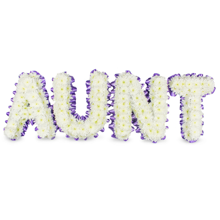 A meticulously composed memorial tribute spells AUNT in large, confident capitals, each letter crafted from hundreds of small, pristine white spray chrysanthemums whose closely packed petals create a smooth, cloud-like surface. The tiny yellow hearts of some florets show through in places, adding natural depth and a faint, warm punctuation to the otherwise pure white field. Around each letter a deep purple satin ribbon is applied as a ruffled outline: the ribbon is pleated and hand-tacked to the letter frames so it sits with neat scallops and a refined satin gleam that complements the flowers rather than overpowering them. Neutral daylight-level lighting highlights the textural contrast between the satiny ribbon and the matte chrysanthemum petals, while soft grey shadows beneath the letters affirm their three-dimensional build and the sturdy internal supports used to keep the tribute upright. There is a subtle green, fresh fragrance to the blooms and an overall impression of calm respect - a design intended to honour memory with grace. As florists working in Grove Park, we design these pieces with practical care: secure wiring, balanced weight and a composed silhouette suitable for placement beside a casket, at a memorial table or at a graveside. Grove Park Florist prepares each commission in our local workshop, and we can arrange delivery across Grove Park, to nearby Lee and Hither Green, ensuring this dignified, personalised floral message can be presented with the quiet reverence it deserves.
