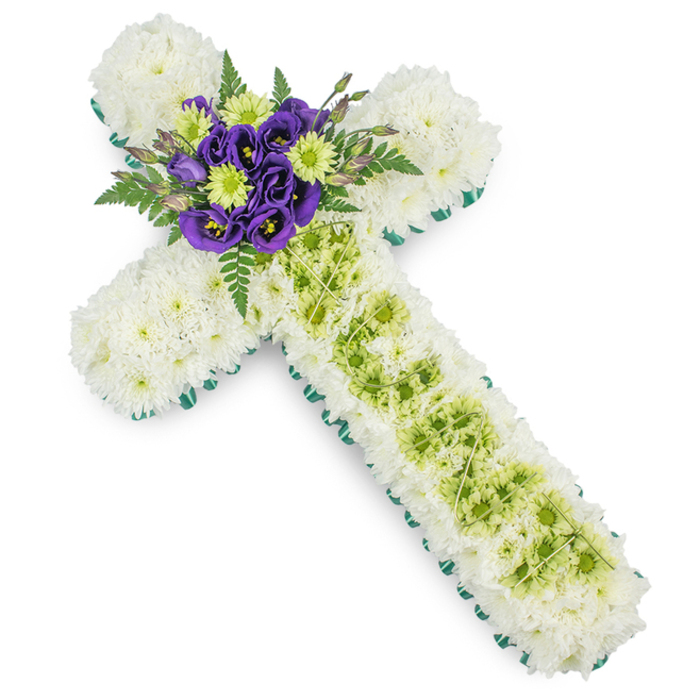 A meticulously crafted funeral cross is captured against a pure white background, its floral details and structured form evoking the calm, reflective tone often requested for services in and around Grove Park. The entire surface of the cross is quilted with white spray chrysanthemums, each blossom carefully placed so that no gaps show, creating a continuous, softly textured field of petals that communicate purity, peace, and a gentle farewell. Framing this expanse of white, a slender band of bright green ribbon or closely laid foliage follows the contour of every arm and curve, giving the Christian cross shape a clear, defined edge and introducing a hint of springlike freshness, much like the green verges along local residential streets. Down the length of the vertical arm, a central feature of lime green button chrysanthemums has been inset, the cluster of tiny, rounded blooms arranged in subtle undulations that create a sense of depth and movement. Over this lime green panel, delicate strands or wires in a slightly paler green form an understated criss-cross pattern, adding visual interest that is only fully appreciated up close, a quiet nod to modern floral design. At the intersection of the horizontal and vertical arms, a focal cluster of deep purple lisianthus anchors the piece, their velvety petals and darker centres bringing richness and emotional weight to the tribute. These purple blooms are highlighted with small lime green chrysanthemums that mirror the central stripe below, while arcs of dark green fern fronds emerge from behind, softening the outline and adding a natural, leafy grace. Crafted in the thoughtful style of Grove Park Florist, this cross suits church altars, crematorium chapels, or gravesides, offering a dignified, faith-filled expression of sympathy and remembrance.