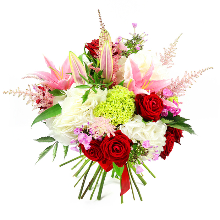 Set against a simple white background, this opulent hand-tied bouquet feels like a moment captured just after a florist in Grove Park has finished adjusting the final stem. Rich crimson roses punctuate the design, their velvety petals wrapped in tight spirals that give each bloom depth and intensity. Standing proudly among them are tall pink lilies, some fully open with broad, satiny petals edged in deeper shades of pink and streaked with softer tones towards the centre, others held in elegant buds that suggest a slow, graceful unfurling and delicate perfume. Cradling these focal flowers are generous clusters of ruffled white blooms, reminiscent of full hydrangeas or large carnations, creating a pillowy base that adds volume and a sense of gentle luxury. At the heart of the bouquet, a rounded cluster of lime green dianthus or Green Trick carnation draws the eye with its unusual, tufted texture and vivid, grassy colour, offering a fresh counterpoint to the romantic reds and pinks. Feathery sprays of pale pink astilbe lift from the arrangement in soft arcs, adding lightness and an airy, almost whimsical silhouette that echoes the relaxed greenery found around Grove Park's tree-lined roads. Scattered throughout are tiny blossoms in fuchsia and lavender tones, subtly deepening the palette and rewarding a closer look. Dark, glossy foliage peeks between the flowers, framing the brighter hues and adding natural structure. At the base, the stems are visibly gathered and tied neatly with a slim red satin ribbon, underlining the bouquet's hand-crafted nature and care. The overall effect is one of joyful sophistication and romance, perfect as a centrepiece or a thoughtful gift for special occasions celebrated in and around Grove Park.