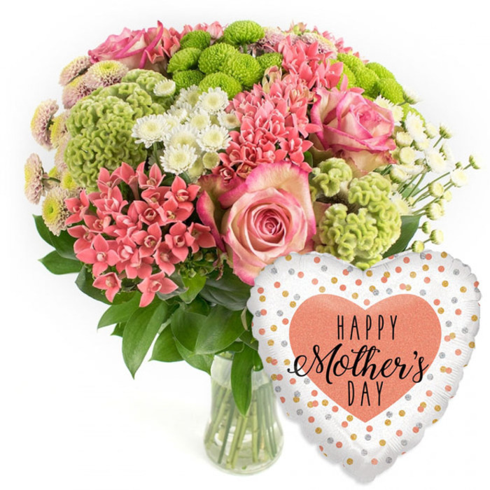 In this photograph, a joyful Mother's Day bouquet and balloon combination is carefully composed against a clean white background, creating a sense of clarity and focus. The bouquet is gathered in a clear glass vase, through which the green stems form vertical lines, adding structure beneath the airy, domed top of the arrangement. At first glance, the soft pink roses draw attention, their petals unfolding in generous layers with slightly deepened pink edges that give each bloom a delicate, almost vintage charm. Around the roses, tight clusters of coral-pink blooms, reminiscent of kalanchoe, contribute a fine, intricate texture; the many small flowers together form cushion-like patches of warm colour. Sprinkled among these are lime-green button chrysanthemums, compact and round, their tufty, detailed surfaces adding modern freshness and an energising pop of lime that contrasts beautifully with the pinks. White daisy-style spray chrysanthemums appear between the brighter hues, their simple, clean petals and glowing centres acting like tiny beams of light, softening and lifting the whole palette. The arrangement is anchored by a generous amount of dark green foliage, the leaves adding depth and shaping the bouquet into a well-balanced, rounded form that feels luxurious yet approachable, much like a hand-tied arrangement you might collect from Grove Park Florist on a walk home by the river. To the lower right side, a heart-shaped foil balloon nestles close to the blooms. Its white or light silver surface is decorated with scattered metallic gold and soft peach dots, giving a confetti effect. At its centre, a solid peach heart holds the message HAPPY Mother's DAY written in black, combining a bold font with flowing script. The overall scene conveys affectionate celebration and gratitude, perfect for Mother's Day deliveries around Grove Park's leafy avenues and family homes.