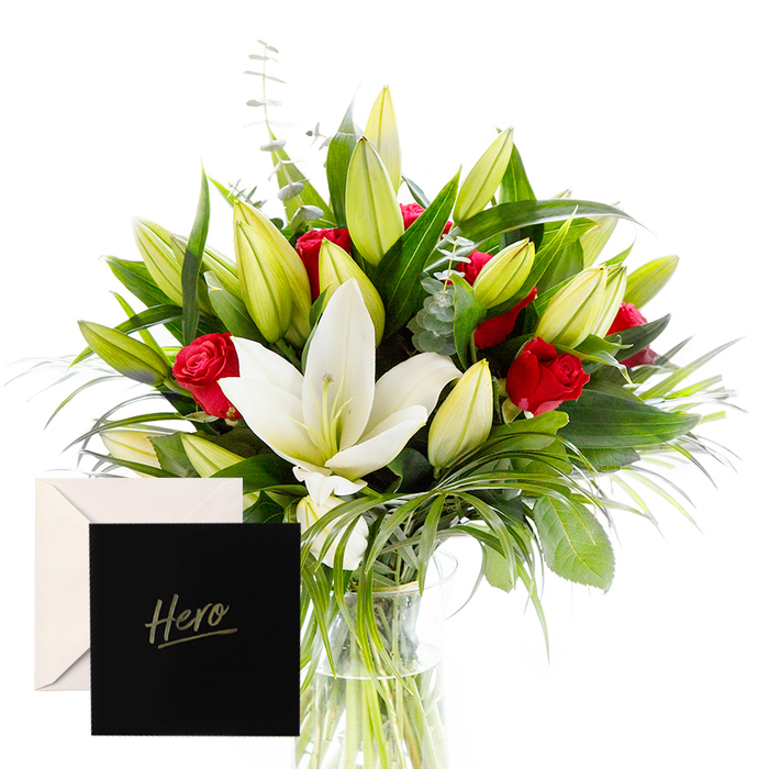 As a local Grove Park florist, I love how bold and serene meet in this arrangement, a harmony that speaks to both celebration and reverence. The white lilies drift at the center, airy and luminous, their satin petals drawing the eye with quiet confidence. Surrounding them, lush green leaves form a cooling ring, their texture ranging from satin to glossy, the kind that catches sunlight and returns it with a soft gleam. The red roses punctuate the design with sudden warmth, each bloom a compact jewel that carries admiration and respect. The overall palette-crisp white, deep ruby, and verdant green-evokes a forest glade washed by morning light; unopened lily buds sit like promises of new chapters yet to unfold.
In this gentle, natural light, the bouquet feels alive, almost hum with contemplative energy, ready to honor someone's strength or mark a significant achievement. The accompanying card marked Hero ties the gesture to a purpose larger than beauty alone, making it a meaningful keepsake as well as a momentary delight. The bouquet rests in a clear glass vase, with the arrangement arranged to echo the rhythm of the city's streets around Grove Park-quiet lanes, bustling markets, and the green spaces of Mountsfield Park not far away. It can be delivered across SE12 and neighboring wards, a reliable token of gratitude that arrives fresh and thoughtfully prepared by Grove Park Florist. In every leaf and bloom, you feel the care of a local team who understands this neighbourhood, ready to bring beauty to life on the doorstep.