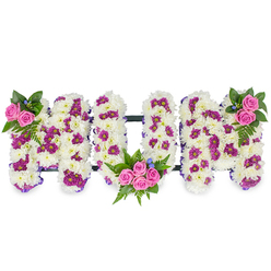 Presented on a crisp white background and photographed in soft studio light, this bespoke sympathy tribute spells out MUM in large, sculpted capital letters made from dense white chrysanthemums. The chrysanthemums form a plush, tactile field whose velvety surface captures the eye and suggests purity and calm. Interwoven across that white base are clusters of deep purple and magenta spray blooms that create gentle contrast and a subtle patterned rhythm across each letter face. Bright pink spray roses act as emotive focal points: a delicate cluster crowns the upper left of the first M, a fuller bouquet of four to five roses is cradled in the lower curve of the U, and a mirrored cluster graces the upper right of the final M. Rich, dark green foliage - including fern fronds and varied leaves - gives weight around each rose cluster and lifts the colour palette, while tiny blue accent flowers add soft, cool highlights among the whites and pinks. A slim dark bar connects the letters horizontally, offering a restrained structural line that keeps the composition unified. Crafted with the kind of careful attention local families expect around Grove Park and Grove Park station, this arrangement by Grove Park Florist conveys sympathy and deep affection - a tactile, floral embrace intended to honour a beloved mother at a funeral or memorial service.