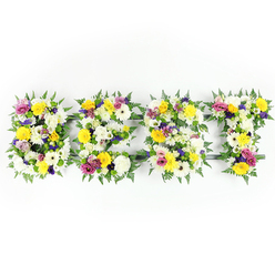 Seen straight-on against a crisp white background, this floral lettering spells BEST with four substantial block letters, each lovingly composed from a dense array of fresh garden flowers and rich foliage. The dominant tones are luminous white and cheerful yellow: large, multi-petaled white chrysanthemums sit like soft cushions beside golden-yellow roses and gerbera daisies that bring sunny clarity to the composition. Deeper notes come from clusters of purple lisianthus or small chrysanthemum varieties in mauve and lavender, while bright magenta spray roses or carnations add sharp, affectionate highlights. Tiny lime-green and ivory filler blooms nestle between the primary heads, creating gentle texture and breathing space, and dark green fern fronds rim the letters with a natural, feathery border that both defines and softens the shapes. Through occasional gaps you can glimpse a dark-green metal support frame-especially visible on the horizontal strokes of the E and T-evidence of the careful construction needed to achieve the even, voluminous surface. The lighting is bright and neutral, chosen to show freshness and vivid colour, and the overall effect is one of respectful celebration: dignified enough for a funeral service yet warm enough for an anniversary or special tribute. As a Grove Park florist familiar with local needs around the High Street and nearby Horn Park, I would suggest this style for families wanting a clear, heartfelt message of remembrance delivered with quiet craftsmanship to services across Grove Park and Lee.