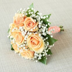 Bathed in gentle, even light, this bridesmaid bouquet radiates quiet sophistication, so familiar to gatherings in Grove Park. Seven or eight fully opened roses, each petal a caress of soft peach and apricot, spiral open in a tightly woven embrace at the bouquet's heart. Clouds of snowy baby's breath, like the delicate blooms seen in the community's well-kept gardens, encircle each rose in a gentle frame, their white faces reflecting the crisp brightness of morning light along Marvels Lane. Lush, green leaves shimmer with subtle gloss, their earthy richness anchoring the pastel pop of roses and guiding the eye across the whole design. The stems are gathered in a peach satin ribbon, smooth to the touch, spiraled tastefully with tiny white faux pearls-evocative of antique wedding charms cherished by families in Grove Park. The bouquet nestles gracefully on an oatmeal-toned linen, the neutral surface highlighting the arrangement's artistry and freshness. There's a faint suggestion of dew-kissed petals, as if just cut from a neighbour's garden in SE12, and the bouquet's gently curved silhouette exudes both poise and approachability. Perfect for weddings, bridal showers, or special moments in Grove Park and beyond, this bouquet is the embodiment of tender love and expert local care, designed to linger in memory as much as in the hand.