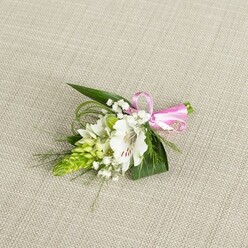 A single, elegant boutonniere lies carefully arranged on a pale beige, linen-like fabric, the soft, woven texture acting as a calm backdrop that brings its colours and details into focus. At the centre, a pristine white alstroemeria unfolds, its petals wide and slightly ruffled, each one finely marked with delicate reddish-brown freckles that draw the eye towards the throat of the bloom. The flower's stamens, faintly dusted with pollen, suggest a sense of living freshness, as if it has just been selected from the conditioning room of a local Grove Park florist. To one side rises a sculptural spike of bright green buds, stacked close together in a cone-shaped cluster reminiscent of Ornithogalum, adding both height and a modern, architectural feel. Around these, light sprays of white baby's breath drift like tiny stars, filling the gaps and giving the piece a soft, airy halo that feels especially gentle and romantic. Dark green, sword-like leaves provide the base, their smooth surfaces and pointed tips grounding the design, while fine strands of grassier foliage arc outwards, introducing a graceful sense of movement. At the right end of the stems, a smooth pink satin ribbon has been tied into a crisp, miniature bow, its sheen catching the even light and adding a joyful pop of colour that hints at celebration. The image is illuminated in a balanced way, free of strong shadows, allowing the subtle interplay of white, green, and pink to read clearly. This small floral piece feels made for a wedding morning in Grove Park, perhaps walking from a nearby home to a church or registry office, quietly capturing themes of new beginnings, tenderness, and thoughtful craftsmanship.