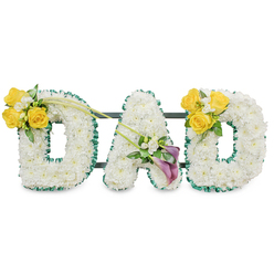 A lovingly made memorial arrangement forming the word DAD, each letter sculpted from a dense blanket of immaculate white chrysanthemums to create soft, rounded block shapes that feel both tender and dignified. Every letter is edged with a ruffled dark green satin ribbon, the rich tone and subtle sheen providing a crisp outline against the pure white blooms and lending a tailored, finished look that holds up well in chapel lighting. Slim dark green metal bars run horizontally behind the letters and are visible in places, a sober structural detail that ensures the display stands together as a single, steady tribute. Cheerful clusters of bright yellow roses crown the outer curves of each D, their petals open and warm, paired with sprays of small white freesias and fresh foliage for texture and fragrance. The central A carries a concentrated, elegant grouping of two deep purple-burgundy calla lilies tucked among tiny white accents, their smooth, sculptural forms bringing a respectful, contemplative note. Long, slender green stems arch toward the centre from the left cluster, introducing a soft diagonal that unites the letters. This piece is crafted with Floristry care typical of a local Grove Park Florist, suitable for delivery to services around Grove Park station, Chinbrook Meadows and neighbouring Downham, and chosen when families want a personal, comforting statement of remembrance in sight and scent.
