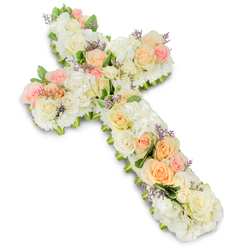 A delicately composed floral cross, intended as a sympathy or funeral tribute, is shown resting on a pristine white surface, its gentle colours evoking peace and remembrance. The cross is fully covered with densely packed blossoms, giving it a rich, cushion-like feel that appears soft even from a distance. A calming trio of hues-white, creamy ivory, and pastel tones of peach and light pink-forms the heart of the design. Large, graceful roses in these colours are scattered in thoughtfully balanced clusters along the cross, their spiralling petals adding depth and a sense of tender movement. Between them, an abundance of white blooms, likely hydrangeas, smaller roses, and other filler flowers, weave together to create a plush, cloud-like backdrop. Tiny accents of lavender or soft purple filler flowers are tucked between the petals, providing subtle flickers of colour that emphasise the intricacy of the craftsmanship. Small sprigs of green foliage peek out around the edges and occasionally through the centre, offering gentle contrast and helping to define the sacred silhouette. The overall effect is one of quiet elegance and spiritual comfort, with bright, even lighting that highlights the natural sheen of each petal and casts a faint, grounding shadow beneath the cross. This is the kind of floral tribute that might be delivered to a Grove Park church, a nearby crematorium, or a family home for a vigil, created by local florists who understand the community's need for dignified, meaningful expressions of farewell. It feels both personal and timeless, a floral cross that softly supports the grieving while honouring a life lived with faith.