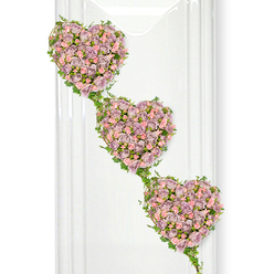 This image presents a beautifully detailed sympathy arrangement composed of three interlinked hearts of roses, arranged in a soft diagonal cascade. Set against a luminous white background, the hearts appear almost to float, their shapes clearly defined by the dense mass of blossoms and trailing greenery. Each heart is richly filled with delicate roses in muted lavender, dusty mauve, and gentle pastel pink, creating a layered, romantic palette that feels both soothing and heartfelt. The roses are placed close together, giving a velvety, cushioned appearance, with clusters of tiny buds nestled among more open flowers to add dimension and visual rhythm. Around and between the hearts, slender strands of ivy weave gracefully, their small, glossy leaves highlighting every curve and providing a fresh green frame that ties the three hearts into one continuous design. These living vines suggest connectedness and the way relationships carry on even after a final goodbye. The clear, even lighting is similar to the soft daylight that might filter into a quiet home in Grove Park, near the tree-lined paths and Victorian houses, or into a calm chapel by the railway. Subtle vertical reflections at the side hint at glass panels or a polished display surface, adding a sense of careful presentation suitable for the front of a funeral service. The mood is tender, reflective, and dignified, ideal for sending condolences or for families choosing a floral piece to lay beside the coffin of someone they adored. It speaks of unity, remembrance, and love that lingers long after the ceremony is over.