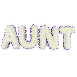 Here a personal message is made tangible: the word AUNT rendered in bold, uppercase letters and entirely formed from tightly clustered white spray chrysanthemums. The blooms feel almost feather-light to the eye, their small, ruffled petals creating a soft, cushion-like texture while tiny pale yellow centres offer a whisper of warmth within the white field. Each letter is bordered with a rich purple satin ribbon, carefully pleated to produce a refined ruffled edge that both outlines and supports the floral silhouette. The ribbon's sheen provides a gentle counterpoint to the matte petals, lifting the composition with a quiet dignity. Studio light washes over the tribute in a soft, even glow, revealing subtle grey shadows under the letters that suggest depth and a real-world presence on a white surface. There is a clean, green fragrance to the chrysanthemums - fresh and lightly dewy - which threads through the arrangement like a comforting memory. Made with thoughtful precision by florists accustomed to delicate commemorations in Grove Park, this piece balances sturdiness and tenderness: the letters rest on firm frames while the flowers keep a compassionate softness. Intended as a sympathetic tribute for funeral services or memorial gatherings, the design communicates respect and lasting affection, a visual embrace for grieving families. Local delivery across Grove Park and neighbouring streets is offered to make this bespoke memorial accessible to those arranging tributes close to home.