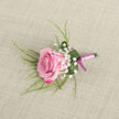 Set against a softly textured, neutral background that resembles light beige linen, this pink rose boutonniere appears as though it has just been laid down before being handed to a groom at a Grove Park wedding. The rose itself lies at a slight diagonal in the lower left, its petals arranged in a gentle spiral from a tightly furled centre that glows with soft, baby-pink tones. As the petals unfurl outward, the colour intensifies into deeper shades of fuchsia and magenta, creating a rich gradient that draws the eye and lends a feeling of depth and romance. Nestled around the rose are fine sprays of white baby's breath, their tiny, cloud-like blooms dancing lightly against the pink and bringing an air of purity and celebration, much like confetti floating outside a ceremony near Grove Park or Chiswick. From behind and beneath the flower, slender, grass-like shoots of greenery extend and curve delicately toward the upper right, giving the design a natural flow, as if a soft breeze from the Thames had brushed past. A single, broad green leaf is carefully curled around the base of the rose, forming a tidy collar where a few clear droplets of water cling and catch the light, hinting at the bloom's recent preparation and careful conditioning. The stems are wrapped with a pale pink satin ribbon, meticulously wound in smooth, overlapping layers that sit flush and even. At the base, a darker magenta-pink ribbon completes the design with a small, neat bow, providing a two-tone contrast that mirrors the rose's own colouring. Crafted with quiet elegance, this boutonniere is perfect for a groom, best man, or prom guest around Grove Park who wants a single, meaningful flower to mark a special moment.