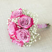 Resting on a neutral, lightly woven beige fabric, this small bouquet feels like a moment of calm just before the festivities begin in Grove Park. The design centres on several beautifully formed bi-colour roses, their petals opening from a soft lavender or pale lilac heart into intense fuchsia and magenta pink at the edges. Each bloom seems to hold a swirl of twilight and sunset within its layers, creating a vivid yet sophisticated colour play. Surrounding and filling the gaps between these roses is a plentiful spray of white baby's breath, its numerous tiny blossoms forming a fine, mist-like texture that softens the bright tones and adds an air of innocence. The stems of the bouquet are firmly bundled and encased in a deep purple satin ribbon, wrapped smoothly to create a sleek handle. Around this handle, a slender strand of glossy white faux pearls coils neatly, giving the impression of a delicate bracelet embracing the bouquet. Placed diagonally with the handle leaning towards the right, the arrangement appears poised for a bridesmaid to pick up on her way to a wedding near the Thames towpath or a prom gathering just off Grove Park Terrace. The muted background ensures the focus remains on the interplay of lavender, pink, and white, as well as on the contrast between the soft petals and the crisp baby's breath. This bouquet evokes feelings of romance, poise, and quiet joy, reflecting the kind of refined floral work a local Grove Park florist might create for intimate ceremonies, engagement photos, or special evenings spent close to home.