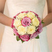 The photograph presents a beautifully composed bridal bouquet, crafted in a classic, rounded style with a lush collection of creamy white, blush-pink, and soft magenta roses. The roses are the clear stars: each bloom is open and full, with velvety petals spiralling outwards in soft layers that give the bouquet a plush, cushion-like feel. Ivory roses are most prominent, providing a tranquil, luminous base, while the pink and magenta roses weave through the design to add warmth and a gentle sense of drama. Interspersed among these are airy clusters of white baby's breath, their tiny blossoms creating a delicate, lace-like texture that lightens the bouquet and draws the eye inward. At the base, a neat collar of greenery peeks out, offering a fresh contrast and evoking the calm, leafy character of Grove Park's residential streets and riverside walks. Gentle, natural light brushes across the petals, highlighting the subtle differences in tone-from creamy vanilla to duskier rose-pink-and adding depth and dimension to the arrangement. Although the image is still, you can almost sense the cool, smooth feel of the rose petals and the soft rustle of foliage as the bouquet is lifted. The imagined fragrance is light and romantic, a soft rose scent that would blend beautifully into a wedding morning at a local Grove Park venue. Overall, the bouquet reads as graceful, balanced, and quietly confident-an elegant floral expression of devotion and new beginnings, perfectly suited to accompany a bride from ceremony to celebration.