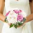 Captured here is a serene and romantic bridal bouquet, the kind you could imagine being carried along Grove Park's quieter lanes on the way to a riverside ceremony. At its core, generous creamy peonies command attention, their petals unfurling in soft, rounded layers that look almost weightless, like folded satin. Surrounding these are refined roses in muted dusty pink and soft violet shades, each bloom carefully placed so that the colours blend seamlessly rather than compete. Fine wisps of gypsophila emerge between the larger flowers, their tiny white blossoms lending an ethereal, airy quality, reminiscent of a veil or a light morning mist over the Thames. Encircling everything, rich green foliage provides a natural frame, the leaves smooth and full, enhancing the pastel tones and giving the bouquet a grounded, organic feel. The design is compact and deliberately structured, clearly hand-tied so it nestles snugly in the bride's hands without feeling heavy or fussy. It has the quiet composure of a bouquet created by a florist who understands both tradition and modern taste, perfectly suited to an elegant Grove Park wedding. One can almost sense the cool stem wrap, the slight rustle as the bouquet is lifted and turned for photos, and the gentle fragrance that accompanies each step down the aisle. The effect is one of understated luxury and deep calm, an arrangement that mirrors the peaceful, leafy character of Grove Park while celebrating love, harmony, and lasting commitment.