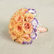 Captured from a slightly raised viewpoint and placed on a warm, textured beige fabric, this bouquet feels like a quiet promise held close. The centre is a perfect, rounded cluster of peach and soft orange roses, each blossom unfurling in a careful spiral that seems to cradle light within its velvety folds. Against that warmth, white lisianthus with their uniquely ruffled petals-each rimmed in a deep violet-introduce a cool, contemporary accent that heightens the roses' glow and draws the eye inward. Scattered throughout are tiny sprigs of baby's breath (gypsophila), their minute, cloud-like blossoms creating delicate negative space and a sense of breathability that lifts the arrangement. The stems are neatly bound in a satin ribbon of pale peach-coral, running down to the lower right where it is ornamented by a slender coil of cream pearls; the pearls catch the light in soft glints, adding an intimate, heirloom detail. Light here is soft and directional, the kind that might arrive through a kitchen window near Grove Park Station in the early morning, flattening harsh contrasts and rendering surfaces tender and inviting. The tactile contrasts-silky petals, frilly lisianthus, feathery baby's breath, smooth ribbon, and cool pearls-make the bouquet as pleasurable to hold as it is to look at. Suited to weddings, vow renewals, and intimate anniversaries, this design reads as quietly joyful and carefully considered, a bouquet chosen for its romance, texture, and ability to evoke memory.