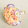 From a slightly elevated viewpoint this bouquet lays gracefully on a pale beige linen surface, the fabric's subtle texture adding an earthy backdrop to the blooms. At its heart sit plush apricot-peach roses, their velvety petals curling in layered spirals that suggest warmth and tenderness; the peach shades slide gently into blush pink at the petal edges. Cooling the composition, white lisianthus with frilly petals are rimmed in a violet-purple tone, each blossom revealing a hint of yellow at its centre and introducing a lively, contemporary accent. Threads of baby's breath are woven throughout like a soft mist, their tiny white points lightening the arrangement and allowing the main flowers to breathe. The bouquet's handle is bound in a matching peach ribbon, meticulously wrapped and embellished with rows of tiny cream pearls that add a refined shimmer and a tactile luxury when held; the green stems are trimmed evenly at the base. Bathed in soft natural light, the petals show delicate sheen and texture, and the overall impression is one of calm elegance-perfect for a wedding, an intimate celebration, or a thoughtful congratulations. Delivered locally across Grove Park and nearby Lewisham streets, this bouquet evokes the quiet corners of the neighbourhood-from morning walks beside the Nature Reserve to small gatherings in community gardens-carrying an aroma of fresh roses and a feeling of handcrafted care.