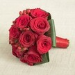 Resting on a subtle cream-coloured linen, a compact bouquet of rich red roses and sparkling hypericum berries radiates warmth and celebration. Each rose is at its best-petals gently open to reveal layers of vivid, velvet red, brushed by even daylight. Between the blooms, rounded berry clusters bring contrast and a pop of festive brightness, their shine highlighting the bouquet's joyful mood. The broad, smooth green leaves encircle the base of the arrangement, adding sturdy structure and deep colour-a nod to Grove Park's tranquil, leafy surroundings. The neat hand-tied stems are finished with a glossy red satin ribbon, crisp and polished for an elegant touch. Created with care by Grove Park Florist, this arrangement evokes romance, fresh beginnings, and the personal style of the local community. It's a perfect choice for Grove Park weddings, heartfelt anniversaries, or spontaneous gestures-each petal and berry a testament to the enduring tradition of floral artistry in Grove Park.