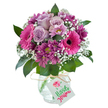 Brimming with colour and personality, this striking bouquet radiates the friendly charm of Grove Park. Arranged with joyful flair, bold fuchsia Gerbera daisies open wide amidst soft lavender roses, each bloom delicately layered and inviting. Deep magenta chrysanthemums, with their subtly textured petals and hints of fresh yellow-green at their centers, gather close, giving the arrangement luxurious depth and movement. Between these, airy sprays of white gypsophila sprinkle a sense of lightness, gently offsetting the vibrancy of the larger blooms. Framing the display, lush, deep green leaves offer contrast and a sense of abundance, much like the leafy stretches along Grove Park's quiet residential streets. The bouquet rests in a rounded clear glass vase adorned with a fine crackled design, reminiscent of artisan touches seen at local fairs. At the neck, a simple raffia tie with a blank white gift tag completes the look, inviting a handwritten note. Uniting artistry and the familiar spirit of Grove Park, this arrangement is prepared for swift, same-day delivery-an ideal choice for birthdays, celebrations, or thoughtful greetings to loved ones throughout the local community.