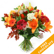 A hand-tied, autumnal bouquet stands upright against a crisp white backdrop, a carefully balanced study in warm tones and seasonal texture. The composition centres on open, trumpet-shaped orange lilies with visible stamens and a few tight buds promising more bloom; around them, plump Gerbera daisies in ruby red and vivid orange form cheerful, circular faces. Creamy white Lisianthus with softly ruffled petals slip between the bolder blooms, lending a cool, delicate contrast, while star-like Astrantia in dusky purple-pink threads its filigree into the arrangement, catching light and adding a faintly whimsical texture. Deep green foliage-likely ruscus or salal-creates a lush base that grounds the colours, and the arrangement's autumn identity is confirmed by several large, deeply lobed oak leaves in varying shades of burnt orange and reddish-brown, their crisp veins and irregular edges giving the bouquet a natural, woodland silhouette.

Stems are neatly gathered and bound with dark twine or raffia, the visible finish signalling a traditional hand-tied technique and the fresh-cut quality of the flowers. The lighting is soft and even, emphasising petal surfaces, the satin sheen of lilies, and the velvety richness of the gerberas without harsh shadow. In the lower right corner a bright orange diagonal banner overlays the image with the bold white text FREE CHOCOLATE, a clear promotional overlay. This arrangement radiates warm hospitality-perfect for autumn birthdays, a Thanksgiving table, or as a thoughtful delivery to brighten a neighbour's day in Grove Park or nearby streets-conveying the scent of green stem and gentle sweetness that lingers after a bouquet is set down.