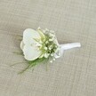 A single white orchid boutonniere rests gently on a softly textured, light beige fabric, its woven surface reminiscent of the relaxed, natural textiles you might find in a Grove Park townhouse near Chiswick High Road. At the heart of the piece, a pristine Phalaenopsis orchid bloom opens with serene grace, its broad, velvety petals a clean, luminous white. In the centre of the flower, a subtle wash of pale yellow glows from the throat, suggesting a just-opened, freshly cut bloom prepared that morning in a local Grove Park florist studio. Surrounding the orchid, tiny white baby's breath flowers form a delicate halo, like wisps of cloud drifting around the central star. Their countless, airy blossoms create a soft, romantic texture that feels perfect for a wedding at a nearby riverside venue or an intimate ceremony tucked away off Grove Park Road. Fine, feathery strands of vibrant green foliage, similar to asparagus or maidenhair fern, peek out from beneath the flowers, lending an organic lightness and a whisper of woodland freshness, as if gathered from the leafy paths near Chiswick House and Gardens. The stems are neatly aligned and expertly wrapped in a smooth white satin ribbon, the finish clean and matte rather than glossy, with a small, understated bow tied near the base to signal where the pin would secure it to a lapel. The gentle, even lighting casts minimal shadows, allowing every petal edge, every bead-like gypsophila bloom, and each strand of greenery to stand out in calm clarity. Overall, the image conveys a sense of quiet elegance and timeless romance, the kind of understated boutonniere a groom, groomsman, or special guest in Grove Park might choose for a refined wedding or formal gathering, where every floral detail is meant to feel both personal and effortlessly sophisticated.