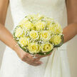 As a florist in Grove Park, I designed this bouquet to embody quiet devotion for a bride who prefers subtlety over spectacle. The palette centres on pale yellow roses - a buttery, pastel tone that suggests warm morning light - each one unfurling in an immaculate rosette formation. Interspersed among them are little sprigs of baby's breath, their minute white blooms hovering like soft confetti to add visual lightness and an airy texture. Encircling the cluster, long curved blades of green grass form a sculptural collar, their smooth arcs providing contrast and an elegant frame that keeps the composition gently contained. Held against a traditional white wedding gown, the bouquet's compact dome complements lace or satin with equal grace; the soft sheen of the petals echoes the gown's fabric and the whole arrangement reads as an intimate statement of hope. Close up, you can almost imagine a faint, sweet fragrance - honeyed petals balanced by the green freshness of the foliage - a scent that feels familiar and reassuring. The arrangement is crafted with the steady hand of someone familiar with local venues around Grove Park station and small parish halls, mindful of scale, sightlines, and how flowers move in a bride's hold. At Grove Park Florist we favour these restrained, emotive pieces for couples seeking a refined, enduring symbol of their day - an accessible, tactile memory that sits comfortably in photographs and in the heart.
