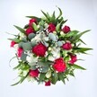 Viewed from directly above against a pure white background, this abundant bouquet appears like a colourful circle of celebration, its blooms gathered tightly together so that every petal and leaf feels intentional. Deep crimson roses nest at the centre, some still cupped in tight buds, others beginning to unfurl in velvety spirals, suggesting romance and quiet devotion. Around them, ruffled carnations in rich fuchsia and ruby red create a soft, cloud-like texture, their intricate petals catching the light and adding a feeling of joyful festivity. Scattered between the warmer tones are clusters of neat white spray chrysanthemums, each daisy-like flower with a clean, bright face that lifts the whole arrangement and lends a crisp freshness. Tiny stars of white gypsophila, or baby's breath, drift through the bouquet like a gentle mist, softening transitions and filling any visual gaps with a delicate, airy veil. Framing this floral heart is a generous collar of greenery: pointed dark green leaves, likely from lilies or alstroemeria, give strong lines and structure, while silvery-green eucalyptus, with its rounded leaves and subtle blue undertone, introduces a cooler, contemporary note. The mix of lush foliage and luxurious blooms feels both classic and modern, as if carefully composed on a florist's bench just off Grove Park's quiet residential streets. The bouquet radiates warmth and vitality, perfect for marking an anniversary, a birthday gathering after a walk along nearby green spaces, or sending a heartfelt thinking of you message to someone in Grove Park. Its full, circular form and harmonious blend of red, white, and green convey love, appreciation, and the promise of shared moments.