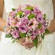 With the tender embrace of a wedding morning, this bouquet speaks quietly of Grove Park's tranquil elegance and the hands of a skilled local florist. Soft lavender and pink roses, opening in gentle spirals, exude a subtle, sweet fragrance, their colours recalling the blush of dawn over local gardens. Green button chrysanthemums, bold and perfectly round, infuse the bouquet with playful energy, standing out like dew-touched foliage along Sutton Court Road. Alstroemeria lilies contribute an exotic flair, their delicate trumpet blooms rendered in blush pink, maroon, and hints of gold, echoing sunlit afternoons in leafy lanes. Cloudlike clusters of baby's breath float between, adding an ethereal lightness and softly linking each element. Framed by lush green leaves, the bouquet sits gracefully against white, embroidered fabric, the bride's gentle hands anchoring the composition and hinting at the emotion of the day. Under natural light, every petal and stem seems to glow, celebrating the beauty and hope that defines weddings in Grove Park. This bouquet, available for same-day delivery and crafted with neighbourhood care, conveys not just a visual delight but a gentle promise - perfect for those beginning their journey together in the heart of this welcoming community.