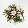 Captured from a direct overhead view against a crisp, pure white background, this bouquet feels like a calm moment of spring light resting on a table in a Grove Park townhouse. At the heart of the arrangement, creamy white and soft ivory roses unfurl in different stages of bloom, from tight buds with a gentle hint of pale yellow at their centres to fully opened blossoms layered with velvety, spiralling petals. Nestled between the roses are elegant stems of alstroemeria, or Peruvian lilies, their slender buds and partially opened flowers washed in mauve, purplish-pink, and lavender tones, some petals brushed with fine green streaks that add a touch of intrigue. Delicate sprays of tiny white gypsophila - baby's breath - thread through the bouquet like a soft, misty veil, lending a cloud-like lightness that softens every transition between flower and foliage. Around the edge, broad, glossy dark green leaves fold protectively, cupping the blooms and giving the design structure, depth, and a sense of freshness that suggests it has just been arranged by hand. The lighting is clean and even, with no harsh shadows, so every petal edge and leaf vein is clearly defined, yet the overall mood remains gentle and serene. It is the sort of refined, romantic bouquet you might send to a friend on Grove Park High Street as a quiet congratulations, or to bring a touch of peace to a riverside flat near Chiswick, expressing comfort, affection, and understated elegance without saying a single word.