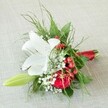 Nestled atop textured beige linen that calls to mind the sunlit table settings of Grove Park's favorite venues, this elegant, intimate bouquet radiates celebratory warmth. The arrangement is anchored by a majestic white lily in full, graceful bloom-its broad petals edged with subtle russet speckles and encircling golden anthers. A deep, rich red rose sits close by, its velvety petals unfurled in a spiral, offering a classic symbol of love and affection. Wispy clusters of delicate white baby's breath interlace throughout, imparting softness and a murmured nod to wildflowers spotted along the Grove Park Green. Eye-catching clusters of glossy red berries punctuate the design, evoking local winter festivity. Various textures of green foliage-airy ferns, shiny leaves, and a solitary fresh lily bud-add fullness and the promise of growth. The bouquet's stems are neatly bound in a luminous red satin ribbon, harmonizing the vivid color story above and rounding out the design with polished grace. This artfully composed floral piece is perfect for milestone celebrations, intimate Grove Park weddings, or as an expressive gift, reflecting both sophistication and the sense of joyful belonging that defines the Grove Park community.