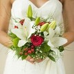 This graceful Grove Park bridal bouquet channels the essence of a handpicked garden gathering-soft, serene, and overflowing with loving intent. Large opulent white lilies bloom at its core, their creamy petals and golden interiors releasing an understated fragrance that mingles with the just-cut green of their buds. Spiralling crimson roses are nestled among them, their velvety curls a vivid declaration of love that echoes down the flower-lined streets of Grove Park. The bouquet sparkles with the surprise of red berries, which peek beneath airy clouds of baby's breath, softening every angle and lending an almost storybook charm. Mossy green dianthus spheres and a tangle of wispy ferns build a grounded, organic foundation, bringing depth and movement like a gentle breeze through Chiswick. The whole arrangement is embraced by the bride's lightly clasped hands set against the delicate textures of her gown-an image resonant with anticipation, peace, and joy. Designed for couples seeking local authenticity and a timeless feel, this Grove Park Florist bouquet truly captures the emotional heart of a wedding day, leaving a lingering impression in both scent and memory.