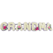 In this image, a tender funeral arrangement clearly spells out GRANDMA using large floral letters, each constructed on a sturdy base and fully cloaked in pristine white chrysanthemums. The chrysanthemums are placed so densely that they create a soft, cushion-like surface, their delicate overlapping petals giving a gentle, almost quilted visual texture to every letter. A narrow lilac ribbon runs neatly around the margin of each letter, shaped into small ruffles and curves that echo the contours of the word, giving the whole tribute a graceful, feminine frame. Three letters-the opening G, a central A, and the final A-carry petite floral posies, where the otherwise white expanse is broken by rounded pink gerberas, layered pink roses, and fresh green foliage. These small arrangements bring moments of colour and life, suggesting memories of laughter, shared celebrations, and treasured family gatherings. The scene is softly and evenly lit, enhancing the purity of the whites and the gentle character of the lilac and pink shades. This floral piece feels deeply personal, the kind of custom design a local Grove Park florist might create for a service at a nearby church or crematorium, perhaps following a family's last walk together through the tree-lined streets of Grove Park or along the river. The overall impression is one of peace, love, and gratitude, capturing in flowers the quiet strength and nurturing presence of a grandmother who meant the world to those saying goodbye.