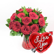 In this image, a romantic gift arrangement is beautifully presented, as if ready to be carried through the quiet streets of Grove Park to someone's front door. At the centre is a sumptuous bouquet of deep crimson red roses, numbering around a dozen or a little more, gathered into a full, rounded shape that suggests abundance and care. The roses vary slightly in their stage of bloom: several are fully open, revealing their layered, velvety petals in detailed spirals, while others are gently opening, their petals still folded inward with a sense of promise. The colour is a rich, passionate red, and it is framed by fresh green foliage that peeks out between the blooms. The leaves are smooth and glossy, their cool green tones providing a striking contrast that makes the roses' colour appear even deeper and more luxurious. These stems are arranged in a clear, ruby-red glass vase, which has subtle vertical fluting along its sides. The fluted lines catch the light, creating delicate highlights and shadows that add texture and elegance to the piece. The vase's warm red tint harmonises with the roses above, giving the entire design a unified, romantic mood-ideal for an anniversary dinner near Chiswick or a Valentine's surprise at home in Grove Park. In the lower right foreground, a gleaming metallic red heart-shaped foil balloon is positioned so that it slightly overlaps the vase and bouquet. Its surface is glossy and reflective, catching bright flashes of light. Across the centre of the heart, the message I Love You appears in graceful white cursive writing. A silver Cupid-style arrow seems to pierce the heart diagonally from lower left to upper right, reinforcing the playful theme of love struck. Against a pristine white background, the vivid reds, fresh greens, sparkling glass, and shiny foil combine into a powerful, classic declaration of love, ideal for any romantic occasion in and around Grove Park.