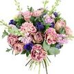 Set against a clean, white background, this hand-tied bouquet appears both generous and carefully controlled, much like a thoughtfully curated Grove Park interior. At the heart of the design, full garden roses in soft blush pink, dusty mauve, and antique rose open luxuriously, each bloom revealing layer upon layer of velvety petals that speak of classic romance. Woven between them, plush carnations create a ruffled tapestry of texture; their centres are creamy and softly blushed, gradually deepening to richer rose, fuchsia, and plum along the delicately feathered edges, adding depth and visual warmth. Among the pinks, deep indigo and royal blue blooms provide strong contrast: some sit as sleek, budded forms, while one open anemone with a dark, almost black heart stands near the front, like a focal note in a piece of music. Slender stems of lilac and pale lavender stock rise through the bouquet, their clustered blossoms introducing gentle height and suggesting a faint, powdery perfume mingled with the clean scent of greenery. Surrounding all of this, glossy dark green rose leaves and softly rounded, silvery eucalyptus create a graceful frame, softening the outline and hinting at a cool, aromatic freshness when the bouquet is lifted. The neatly tied stems are visible at the bottom, confirming it as a freshly made arrangement, ready to slip into a vase on a dining table near Grove Park station or in a light-filled flat closer to the river. With its harmonious blend of romantic pinks, serene purples, and dramatic blues, this bouquet feels suited to anniversaries, heartfelt thank-yous, or quiet moments of reflection shared within the local community.