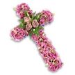 This image shows a graceful floral cross arranged against a crisp white background, the contrast making every petal stand out. The cross is generously covered with flowers in shades of pink, mauve, and soft purple, layered so densely that the piece looks plush and comforting, like a bed of blossoms laid gently in remembrance. At the central point where the arms meet, three open roses in a soft dusty rose and light mauve tone provide a clear focal point. Their petals are full and gently spiralled, creating the sense of a tender heart at the centre of the tribute, echoing the love shared at many quiet goodbyes in Grove Park. Around these roses, slim fern fronds and bright green leaves weave between the larger blooms, injecting vibrant colour and a natural, garden-inspired touch that feels in tune with the area's leafy character. 

From this centre, the arms and base of the cross are entirely filled with trumpet-shaped Lisianthus flowers. They appear in a spectrum of pinks and mauves, some paler, others richer, with a number showing darker centres that add delicate depth. Between them nestle fine filler flowers in pale pink, cream, and soft lavender, while scattered light green buds provide a gentle hint of new life and hope. Just at the outer edges, discreet glimpses of a darker purple ribbon or supporting base peek through, shaping the cross and giving it a subtle sense of structure without detracting from the floral abundance. The overall mood is peaceful and reverent, like a carefully considered farewell created by Grove Park Florist for a funeral, memorial service, or graveside tribute, expressing faith, respect, and enduring remembrance through colour, texture, and form.